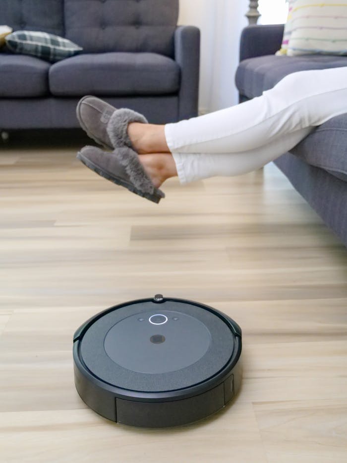 Autonomous robot vacuum cleaning hardwood floors under relaxing person's feet.